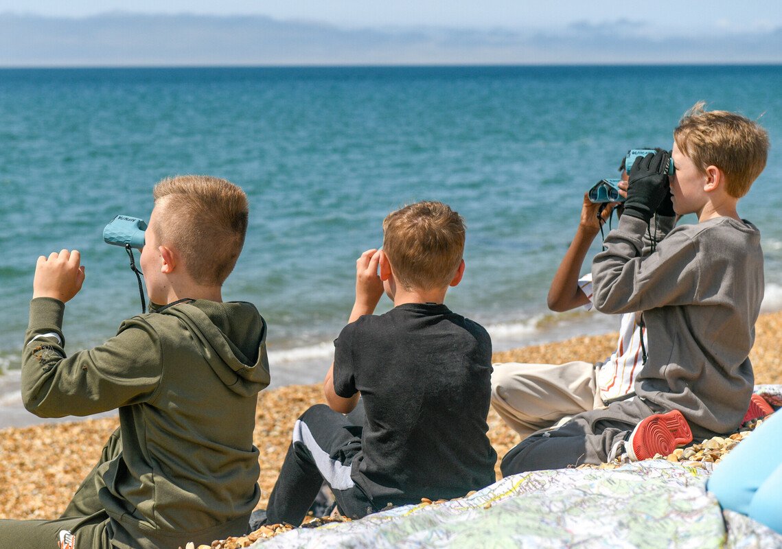 Four young boys with binoculars sat on a blanket and looking out to see 