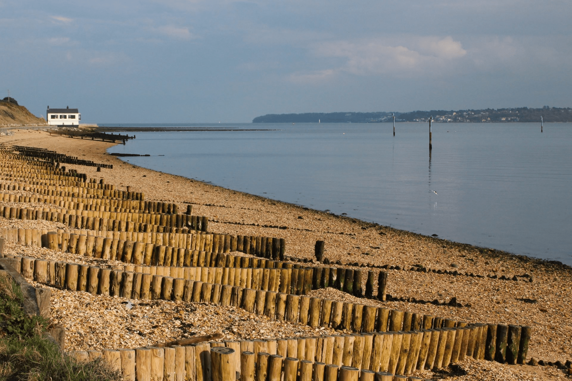 Pebble beach with wooden groynes, calm sea and channel markers, and a white building on the shore at Lepe and Exbury